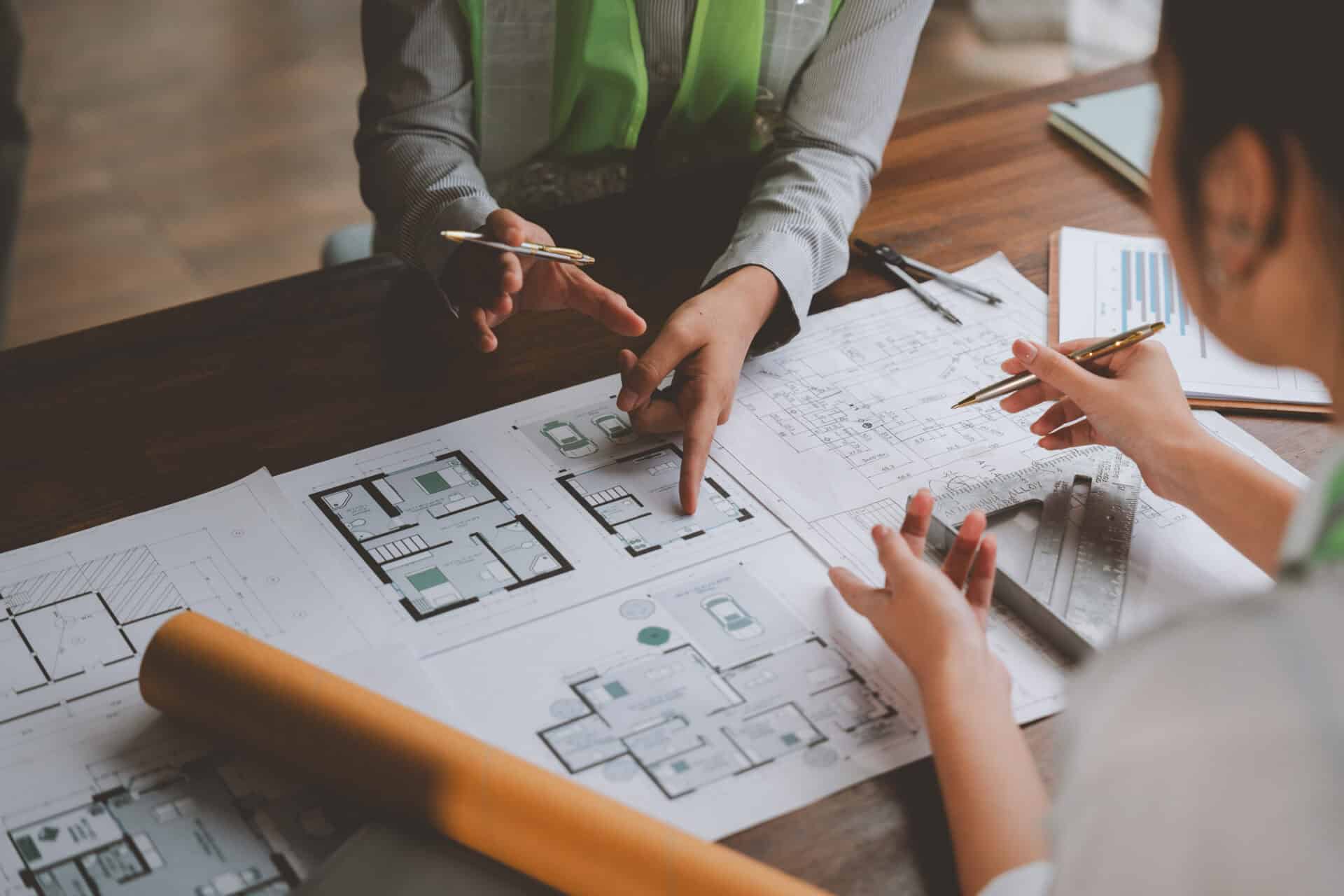 Architects and engineers pointing at building project blueprints during a meeting, discussing details and planning construction